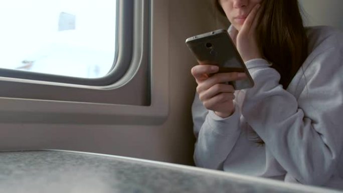 疲惫的年轻女子在火车上看手机视频。双手特写。