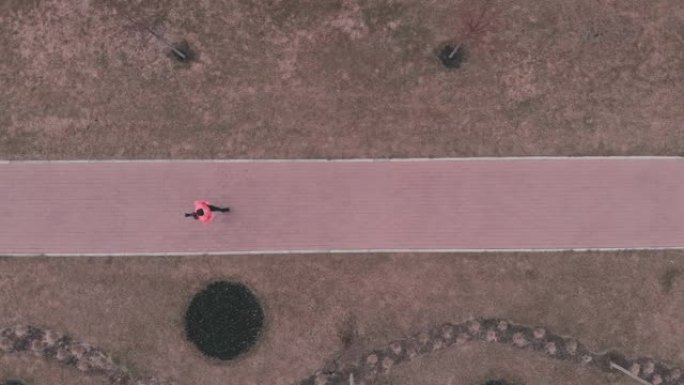 女人在空旷的人行道上奔跑。穿着鲜艳运动服的女运动员沿着行人路奔跑，空中俯视图