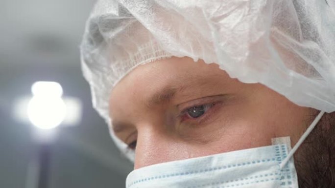 戴着外科口罩的疲惫的外科医生低头看着病人，然后站在监视器或助手一边。手术，从业者，手术室，手术，移植