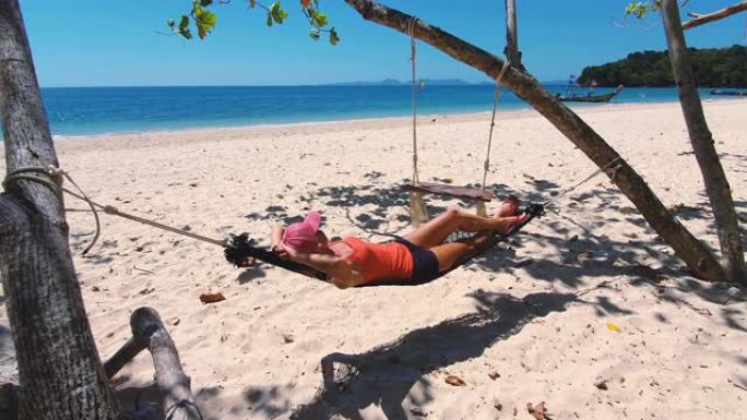 穿着橙色t恤和帽子的女人在吊床上的海滩上。