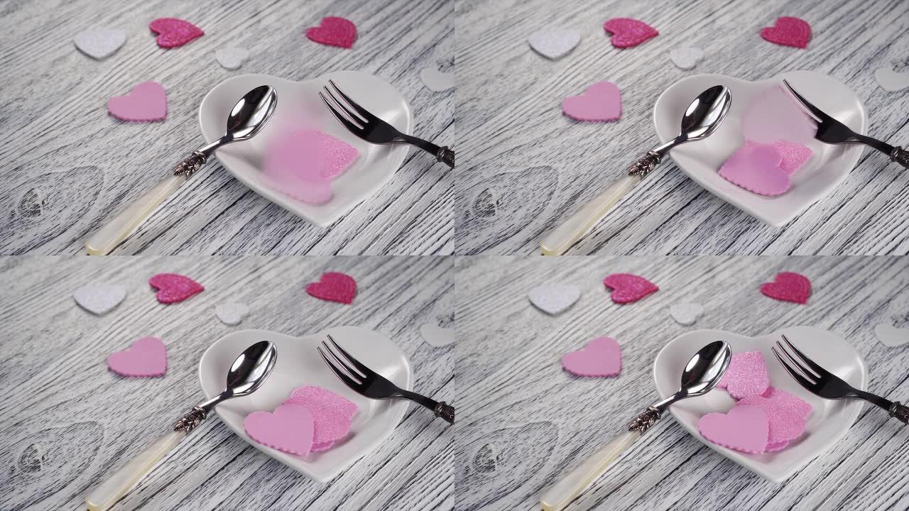 装饰心落在带有甜点叉和勺子的心形盘子上。在木制轻纹理桌上