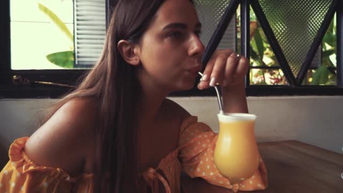 年轻迷人的女人喝新鲜的热带芒果冰沙奶昔果汁使用零废物环保金属可重复使用的草莓素食餐厅。