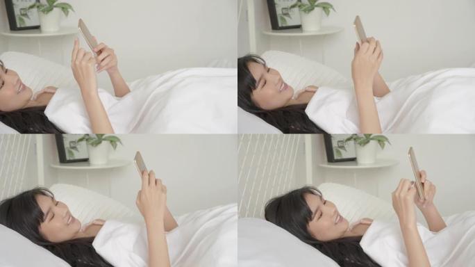 美丽的年轻亚洲女子看着和触摸智能手机放松享受床上的社交网络，女孩聊天信息上网，交流理念。