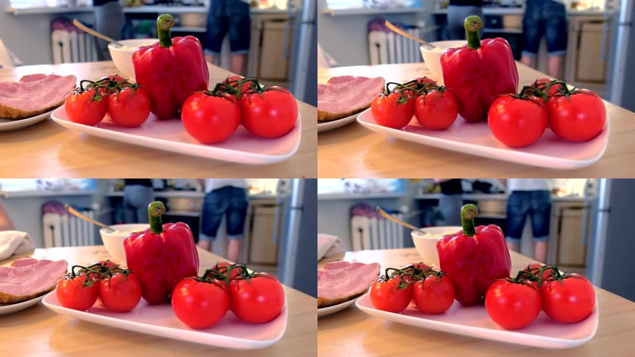 厨房桌子上的胡椒、西红柿和火腿。家人正在家里做饭。