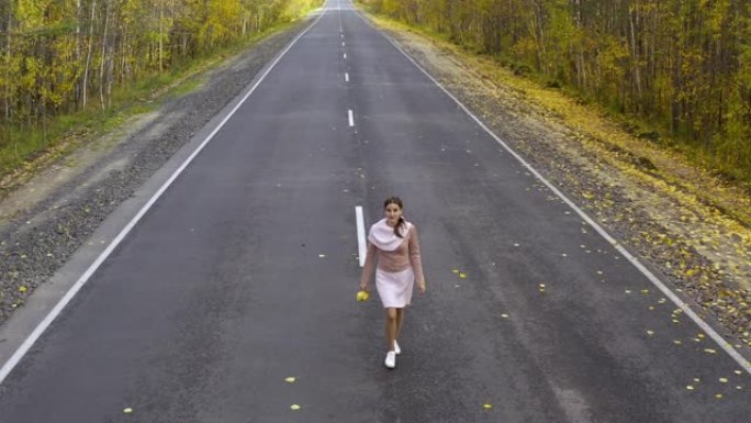 穿着粉红色衣服的女性在秋天森林的柏油路上奔跑和旋转。顶视图