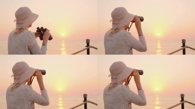 一名年轻女子在远处透过双筒望远镜望去，迎接一个粉红色的梦，坐在朝阳的阳光下的海上码头上