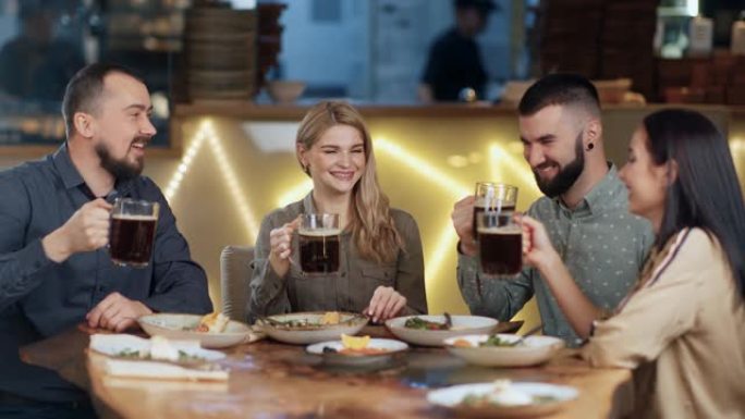 四个朋友在酒吧坐在餐桌旁敬酒马克杯麦芽放松。在红色乌鸦4k电影摄像机上拍摄