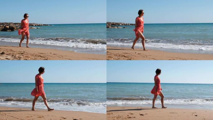 穿着红色短裙的年轻迷人女孩在海上行走。白人黑发女人走在沙滩上。穿着红色泳衣和裙子在海滩散步的年轻女孩