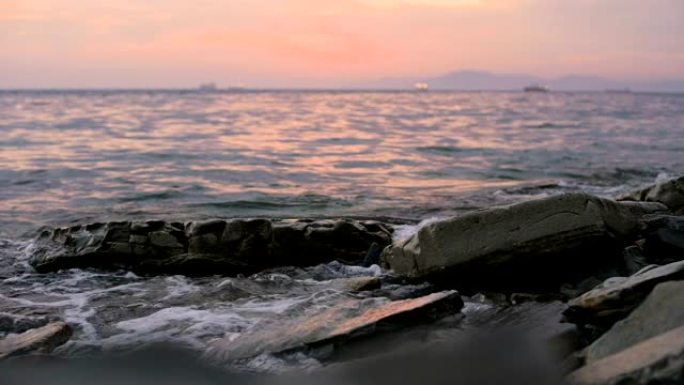 特写慢动作低角度小海浪在岩石海滩上滚动。海边。鹅卵石岩石海滩上的日落