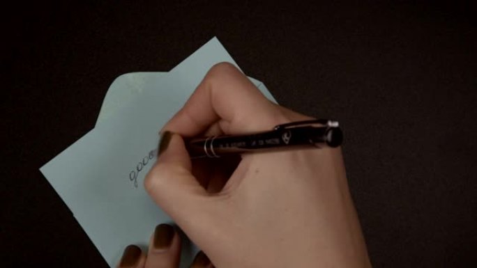 女手在纸上写上笔 “再见”，并将其放在蓝色信封中。离别与过去离别的概念，特写