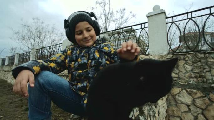 戴着耳机和保暖衣服的男孩抚摸坐在腿上的猫