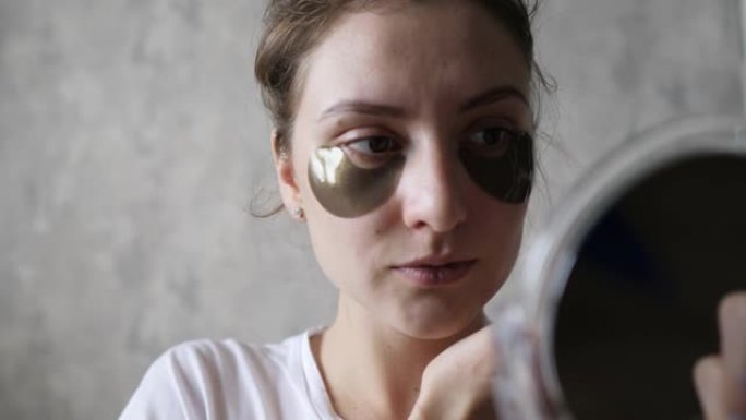 眼睛下的皮肤提升-一个照镜子的健康女孩使用天然化妆品