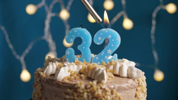蓝色背景上有32号蜡烛的生日蛋糕。蜡烛着火了。慢动作和特写视图