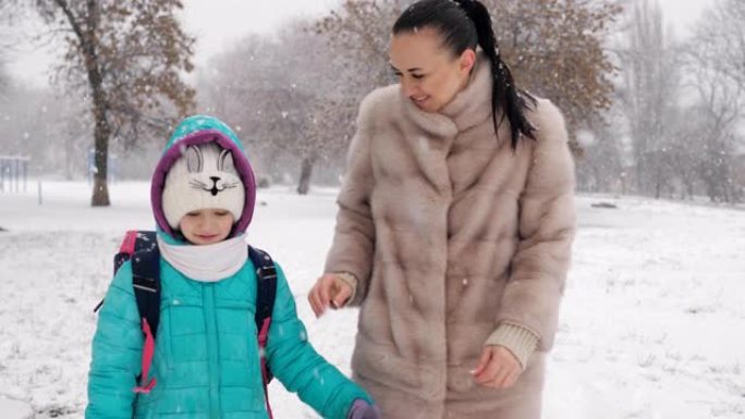 母亲和年幼的女儿在雪地里放学后牵着手回家。