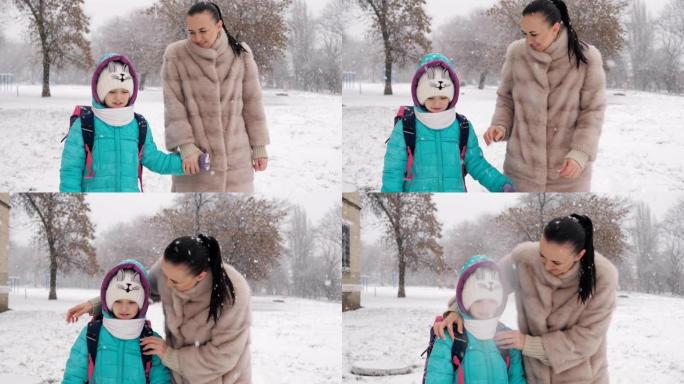 母亲和年幼的女儿在雪地里放学后牵着手回家。
