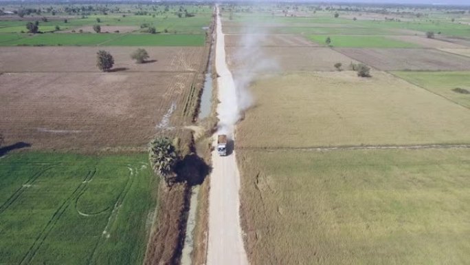 无人机拍摄到建筑卡车在尘土飞扬的道路上穿过稻田