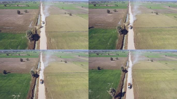 无人机拍摄到建筑卡车在尘土飞扬的道路上穿过稻田