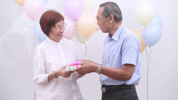 亚洲老年夫妇在家里拿着庆祝生日的礼物。老人在家里一起享受快乐时光。高级家庭在家的概念。