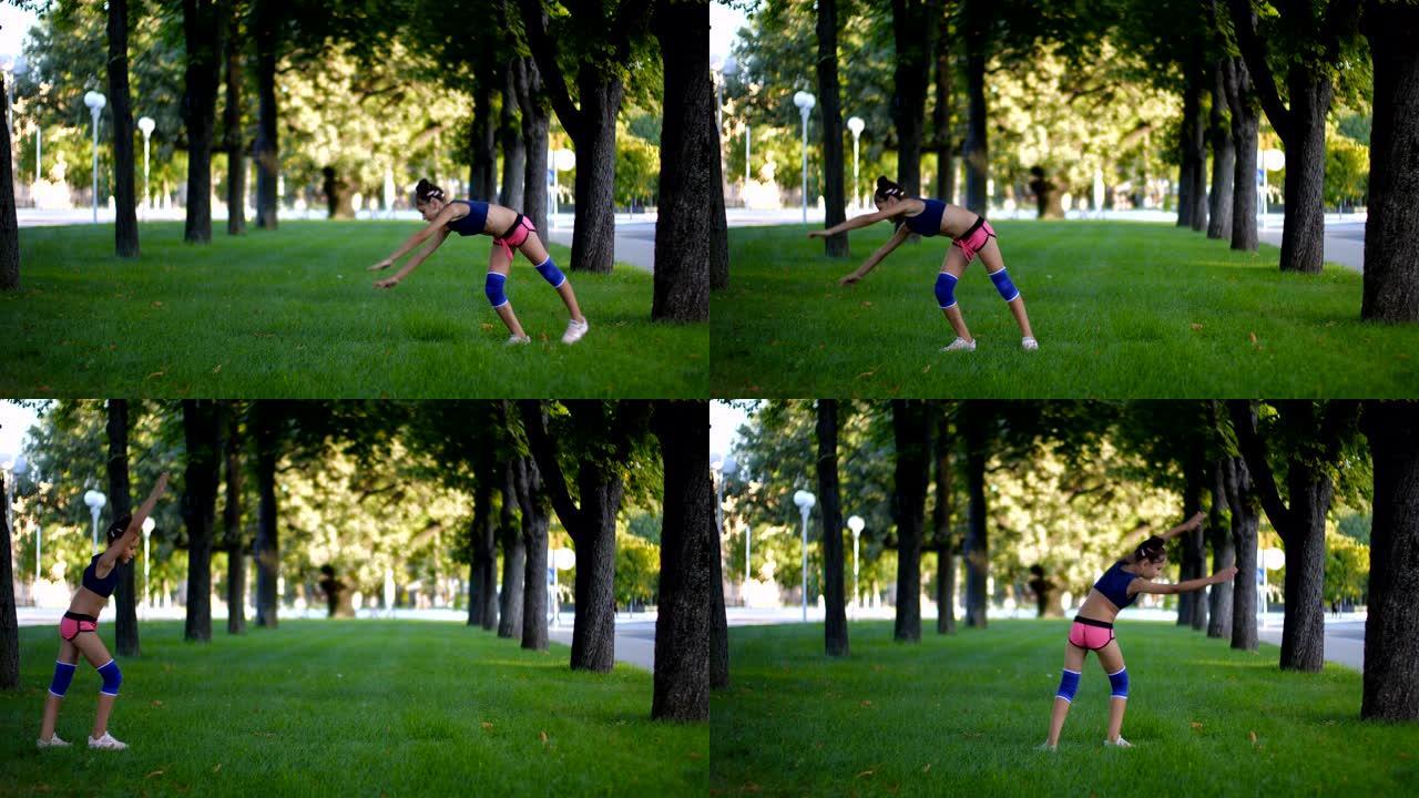 在阳光明媚的夏日，在城市公园的草地上，穿着运动服的七年美丽的白人女孩在草地上练习车轮体操运动。慢动作