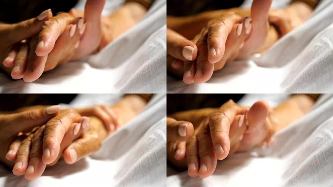 女人温柔地抚摸着母亲照顾她的手。女儿安慰躺在医院床上的年迈妈妈皱巴巴的手臂。向父母示爱的女孩。背景模
