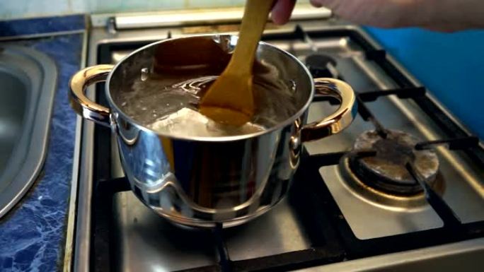 用木勺将盐倒入沸水中。一个金属锅，里面有沸水和少许盐，用于烹饪。