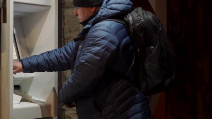男子带背包使用户外atm机在夜间城市街道提取现金