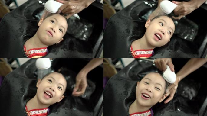 亚洲小女孩在美容院洗头。理发师给她的客户洗头。小女孩有幸福，喜欢洗头。手持镜头，真实生活