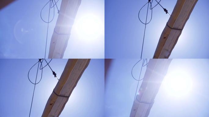用于建造木屋的带原木的起重机。夹。起重机绳索上的悬浮木材在带有阳光的蓝天背景上称重