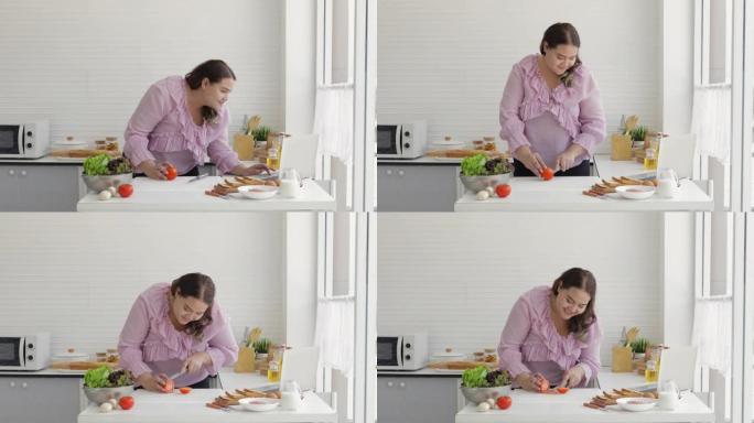 胖女人正在准备西红柿做汉堡，同时在家庭厨房的笔记本上在线观看如何做。垃圾食品和超大号肥胖成熟女性和超
