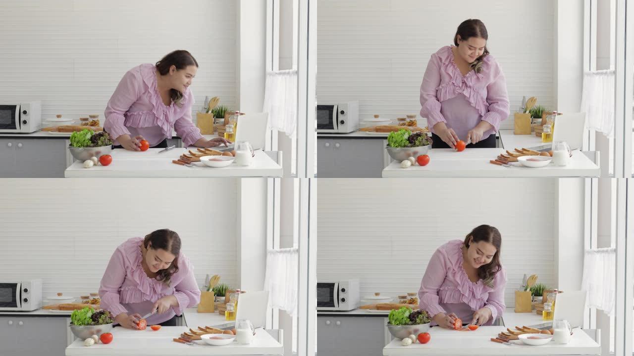 胖女人正在准备西红柿做汉堡，同时在家庭厨房的笔记本上在线观看如何做。垃圾食品和超大号肥胖成熟女性和超