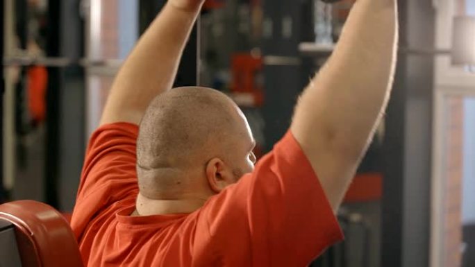 超重男子在健身房举起哑铃的后视图。胖男性锻炼减肥