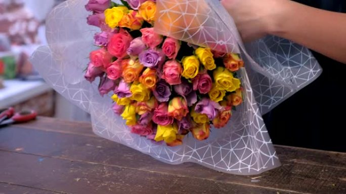 女花店在花店用纸包装玫瑰花束，双手特写。