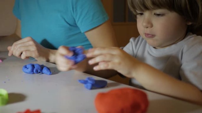 儿童在托儿所的餐桌上对橡皮泥进行建模。儿童男孩和母亲在家里的游戏室玩彩色粘土玩具。年轻的女人和儿子在