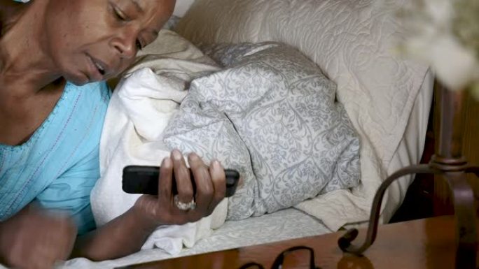 老年黑人妇女躺在床上检查手机