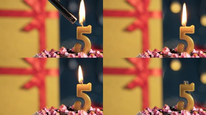 生日蛋糕5号点火器燃烧的金色蜡烛，蓝色背景礼物黄色盒子用红丝带绑起来。特写和慢动作