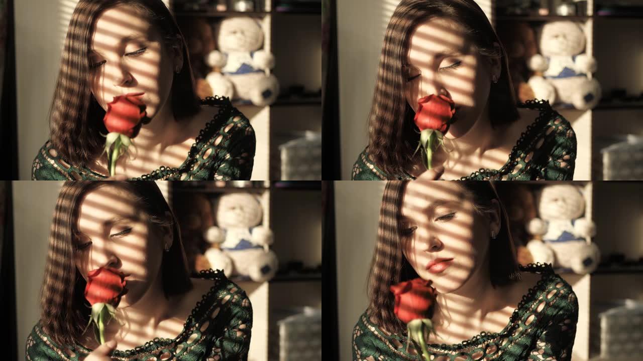 美丽的女孩坐在日落的窗边，爱着红玫瑰，嗅着花。情人节，2月14日，生日，周年纪念日，第一次约会的概念