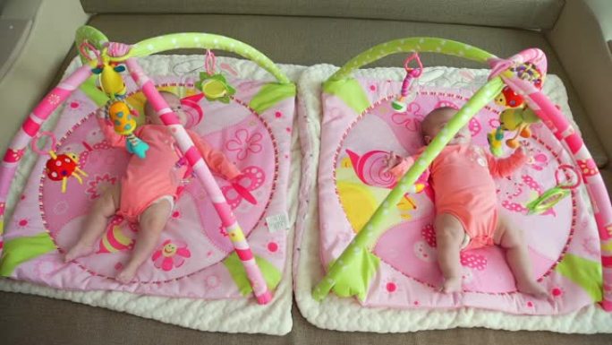 可爱的双胞胎女婴躺在彩色游戏垫上