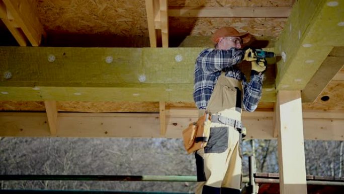 30多岁的承包商工人将绝缘矿棉块连接到房屋元素上。