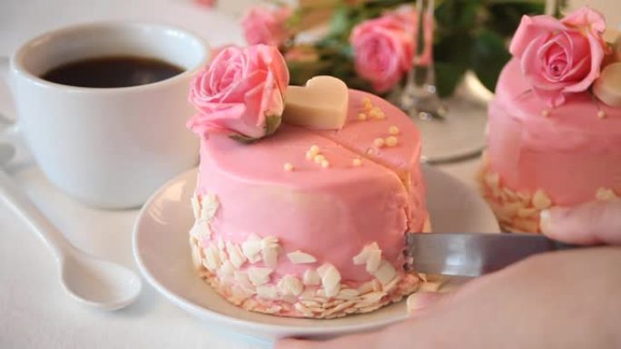 女人用粉色釉切迷你小蛋糕，装饰美丽的玫瑰。背景上的一杯咖啡