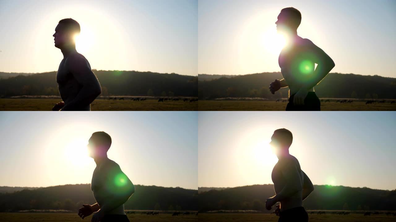 年轻的肌肉男跑过田野与日落的背景。强壮、耐劳的运动员在户外跑步。在大自然中进行士兵运动训练。健康积极