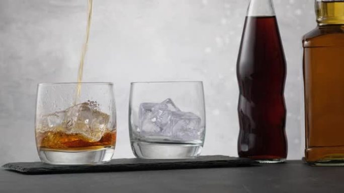 将威士忌倒入带有冰块的玻璃杯中，背景为两瓶可乐