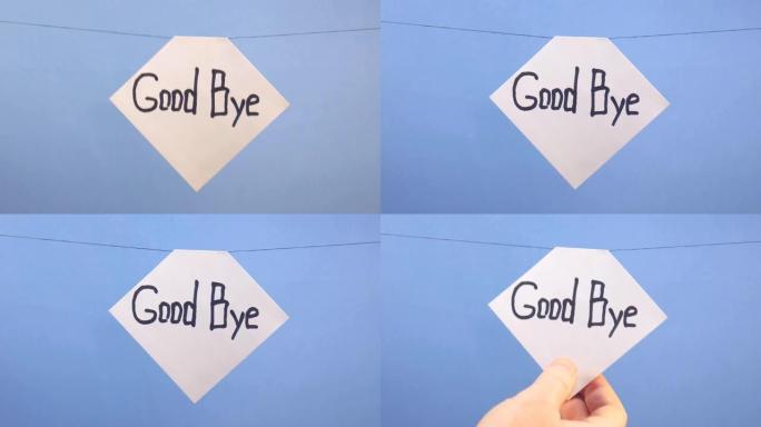 一名男子在蓝色背景上悬挂一张白纸，上面刻有黑色题词 “good bye”