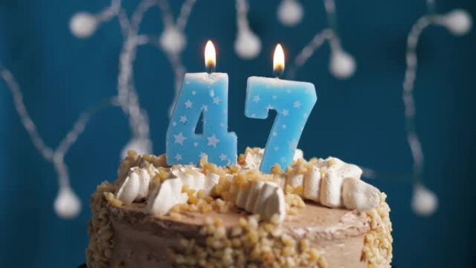 蓝色背景上有47号蜡烛的生日蛋糕。蜡烛吹灭了。慢动作和特写视图