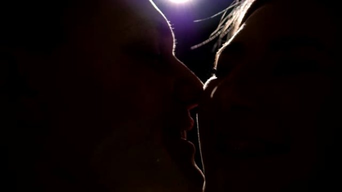 一对在黑暗中恋爱的情侣在他们亲吻的聚光灯下的剪影。