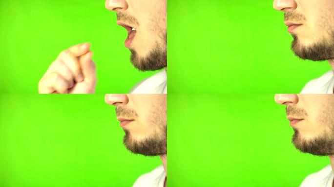 一个大胡子男人的嘴嚼口香糖的特写。框架中侧面的男人将口香糖枕头放在嘴里，并在绿屏背景上咀嚼