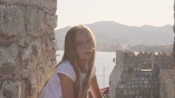 肖像美丽的女孩，在石质堡垒和海洋景观上随风挥舞着头发。旅游女孩在古老的堡垒和海洋背景上寻找相机。