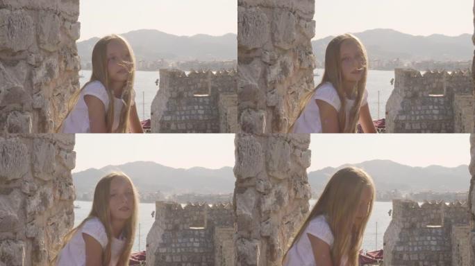 肖像美丽的女孩，在石质堡垒和海洋景观上随风挥舞着头发。旅游女孩在古老的堡垒和海洋背景上寻找相机。