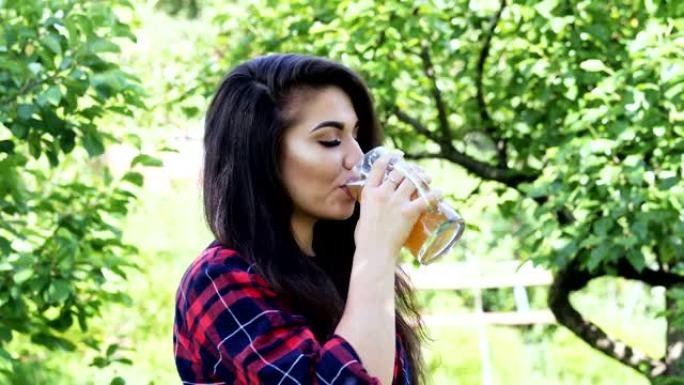 年轻幸福的女人的肖像在花园里喝杯啤酒，止渴