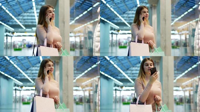年轻女子的侧视图，带着购物袋站在购物中心的橱窗旁边，看着人体模型上的服装，在手机上聊天，向男友要钱，