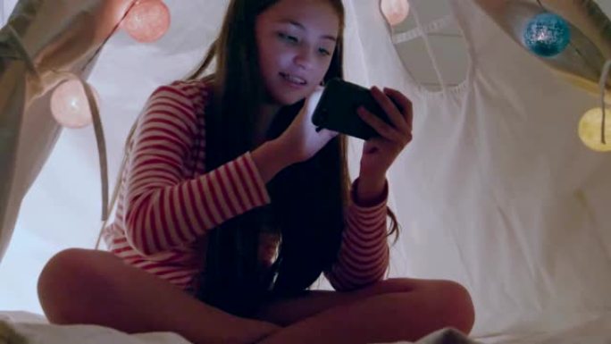 生活方式小女孩高加索人坐在卧室里玩手机装饰彩灯，手姐触摸屏手机